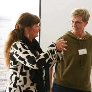 Das Bild zeigt zwei Frauen. Sie unterhalten sich miteinander und gestikulieren. Hinter ihnen sind Pinnwände zu erkennen. Beide Frauen sind Trainerinnen der abb-seminare.