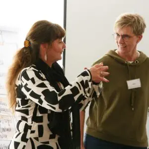 Das Bild zeigt zwei Frauen. Sie unterhalten sich miteinander und gestikulieren. Hinter ihnen sind Pinnwände zu erkennen. Beide Frauen sind Trainerinnen der abb-seminare.