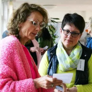 Auf dem Bild sind zwei Frauen zu sehen. Eine Frau hält eine Karte in der Hand. Beide Frauen schauen sich gemeinsam die Karte an.