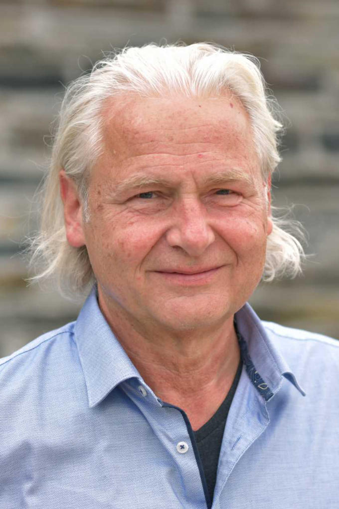 Auf dem Bild ist ein älterer Mann mit weißem, schulterlangem Haar zu sehen. Er schaut freundlich in die Kamera und lächelt leicht. Er trägt ein hellblaues Hemd mit offenem Kragen und darunter ein dunkelgraues T-Shirt. Zu sehen ist Ausbildungsleiter Positive Psychologie Albert Glossner. Er begleitet die Ausbildung bei abb-seminare mit viel Erfahrung, Klarheit und Herz.