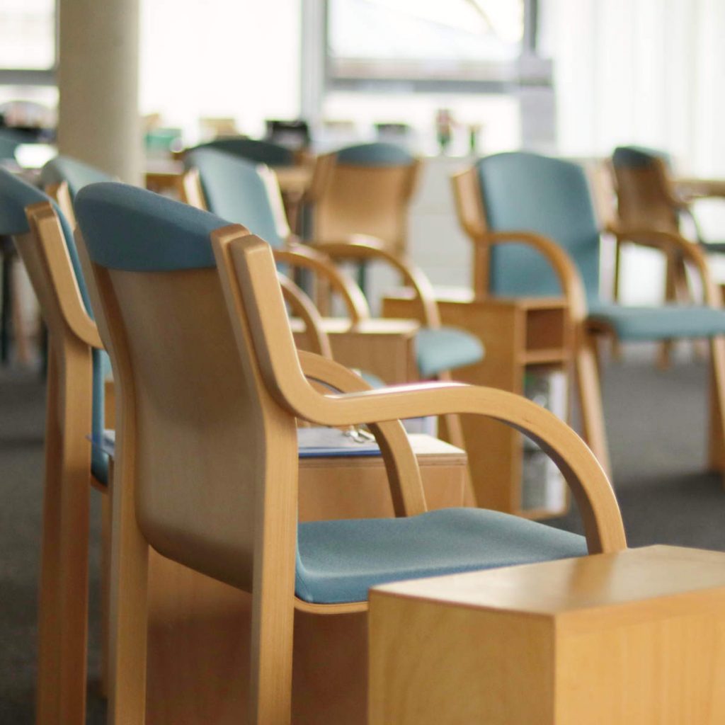 Das Foto zeigt einen Ausschnitt aus dem Seminarraum von abb-seminare in Leipzig. Zu sehen sind die Stühle im Seminarraum aus Holz mit Polsterung. Im Hintergrund ist die Glasfassade leicht zu sehen.